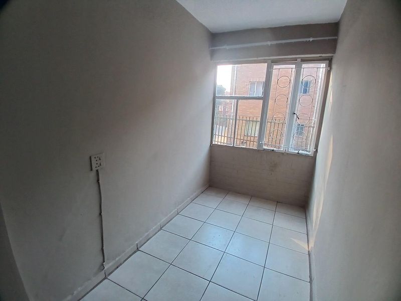 A compact, empty bedroom featuring tiled flooring, a window with security bars, and visible electrical wiring on the wall.