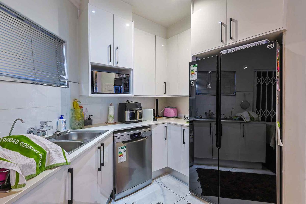 Modern kitchen featuring white high-gloss cabinetry, stone countertops, stainless steel double sink, and integrated dishwasher space.