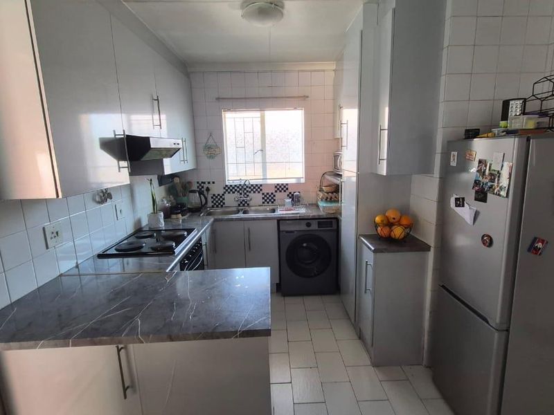 Functional kitchen featuring built-in cabinetry, laminate countertops, electric hob, extractor fan, and tiled finishes with integrated space for laundry appliances.