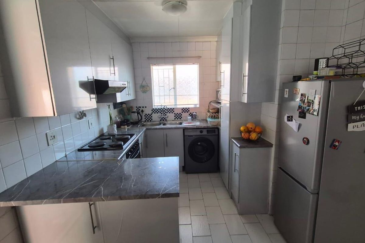 Functional kitchen featuring built-in cabinetry, laminate countertops, electric hob, extractor fan, and tiled finishes with integrated space for laundry appliances.