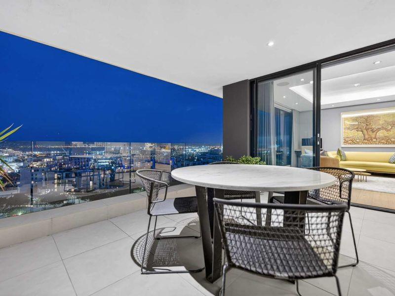 A modern covered balcony featuring a glass balustrade, tiled flooring, and recessed lighting, offering expansive city views and seamless indoor-outdoor flow.