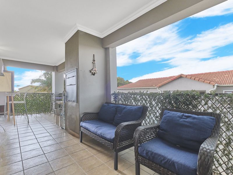 A covered balcony featuring tiled flooring, a built-in braai, and a lattice privacy screen, offering a functional outdoor entertainment space.