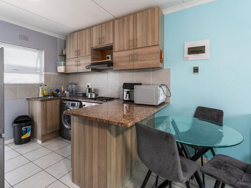 Compact kitchen featuring wood-look cabinetry, granite countertops, tiled backsplash, and integrated appliance space, offering a functional layout for apartment living.