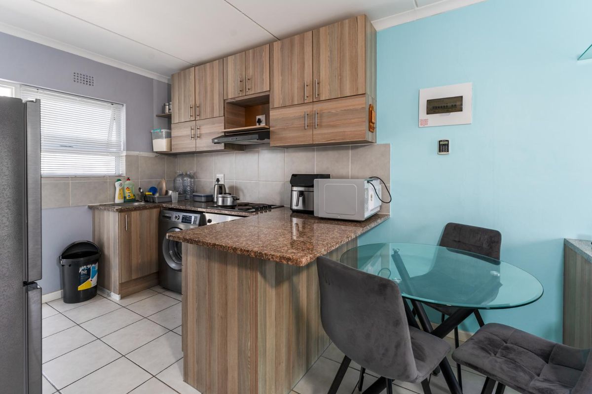 Compact kitchen featuring wood-look cabinetry, granite countertops, tiled backsplash, and integrated appliance space, offering a functional layout for apartment living.