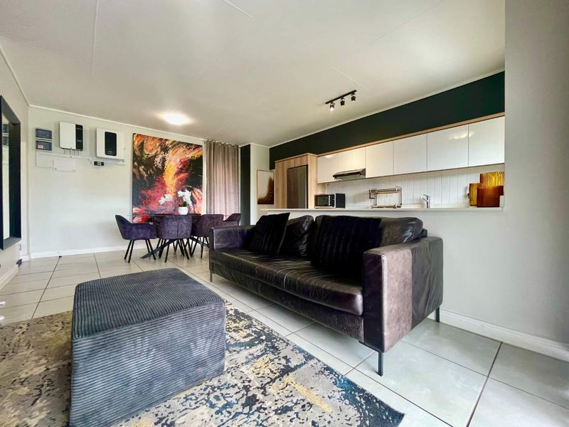 Modern open-plan living area featuring a sleek kitchen with white cabinetry, tiled floors, and a seamless flow into the dining and lounge space.