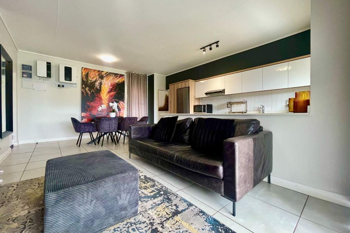 Modern open-plan living area featuring a sleek kitchen with white cabinetry, tiled floors, and a seamless flow into the dining and lounge space.