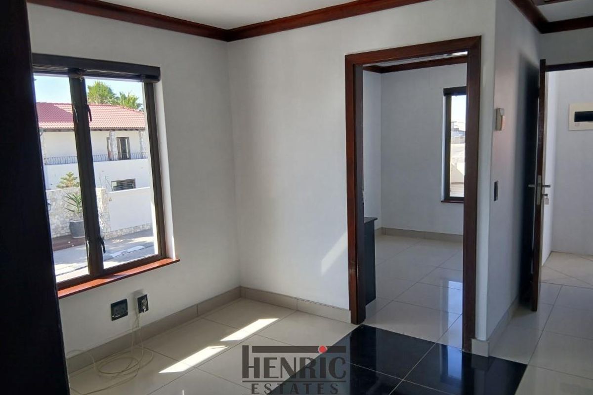 A bright, empty bedroom featuring tiled flooring, dark wood trim, and a doorway leading to an adjacent room.