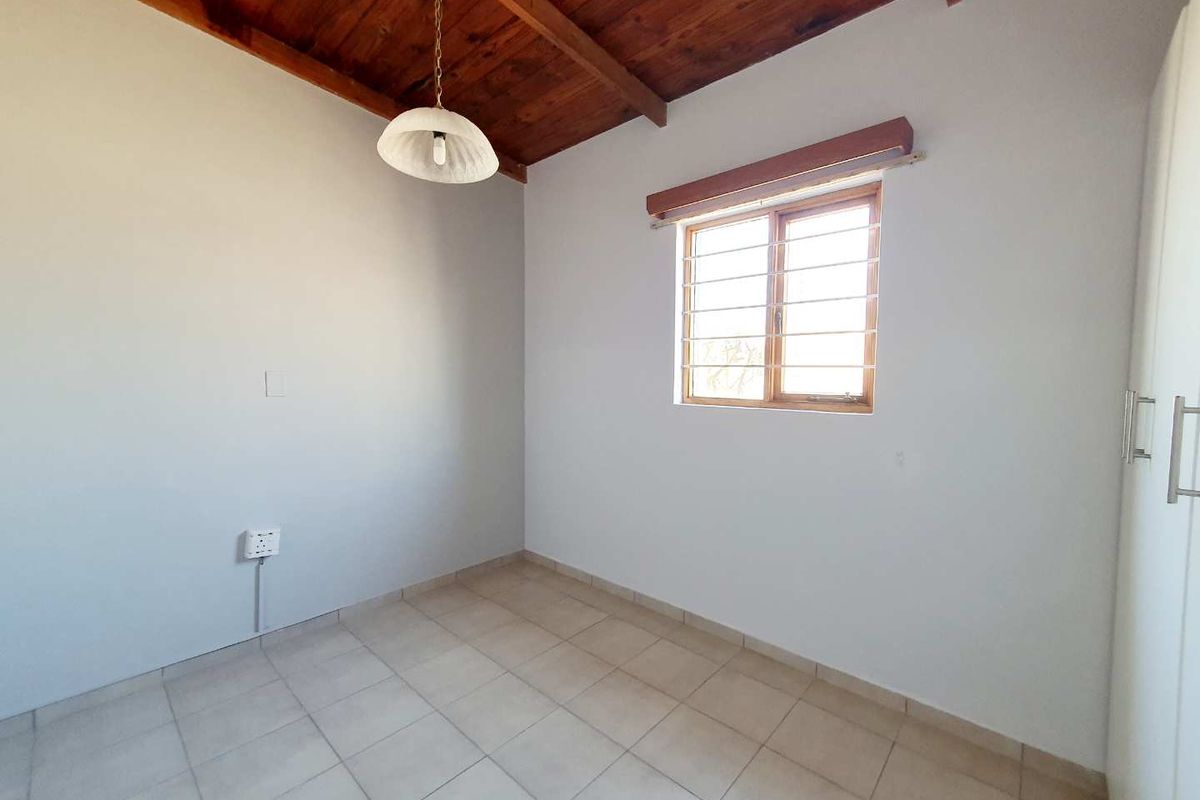 A bright, empty bedroom featuring tiled flooring, a timber-beamed ceiling, and built-in cupboards.