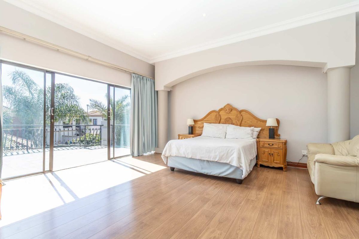 Spacious bedroom featuring laminate flooring, an arched architectural detail, and large sliding glass doors opening onto a private balcony.
