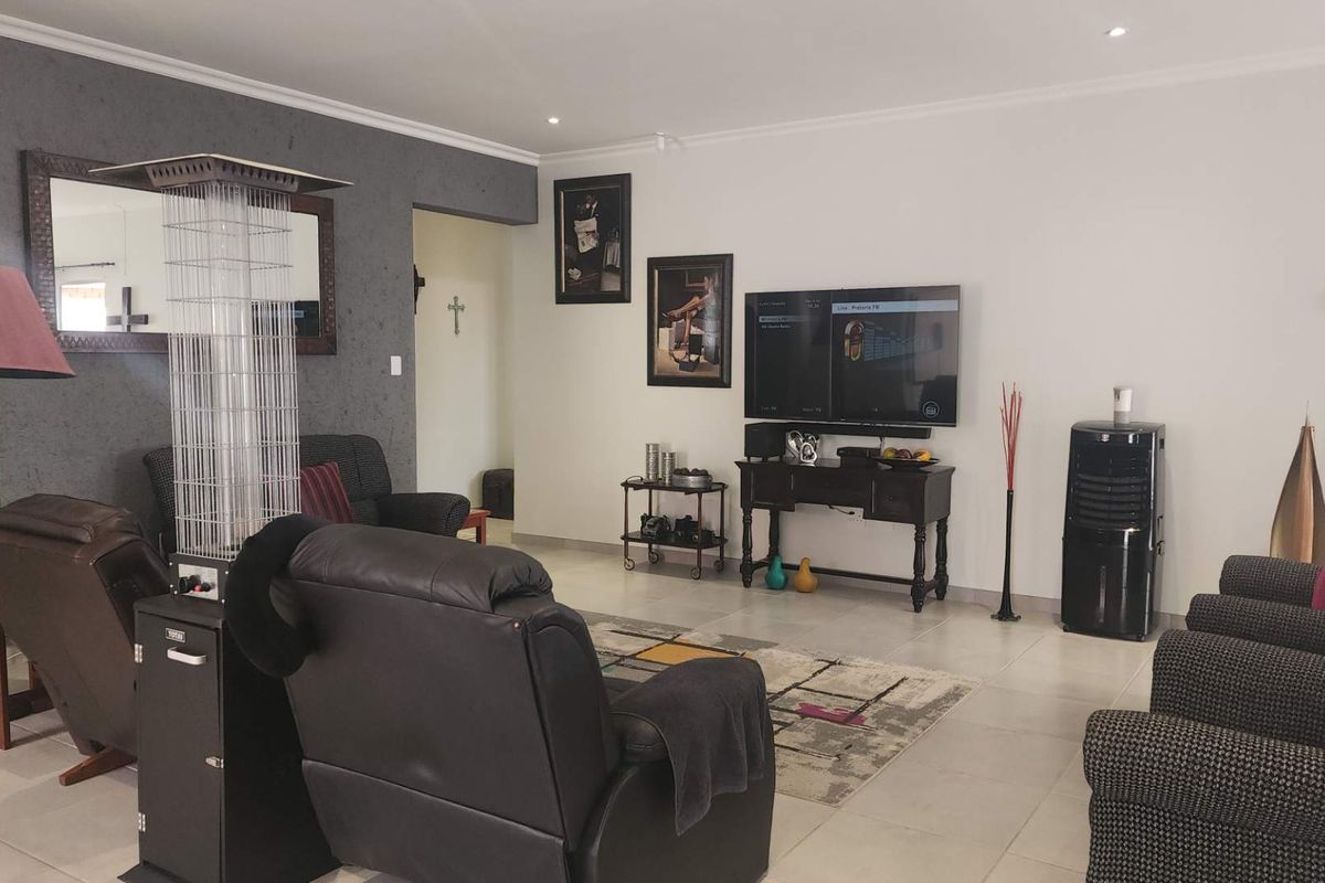 A spacious living room featuring neutral tiled flooring, recessed downlighting, and a textured feature wall.