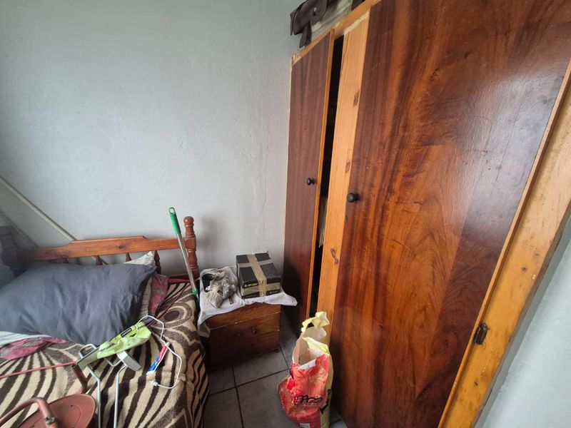 A bedroom featuring a built-in wooden wardrobe and tiled flooring, requiring cosmetic updates to improve the overall condition and aesthetic appeal.