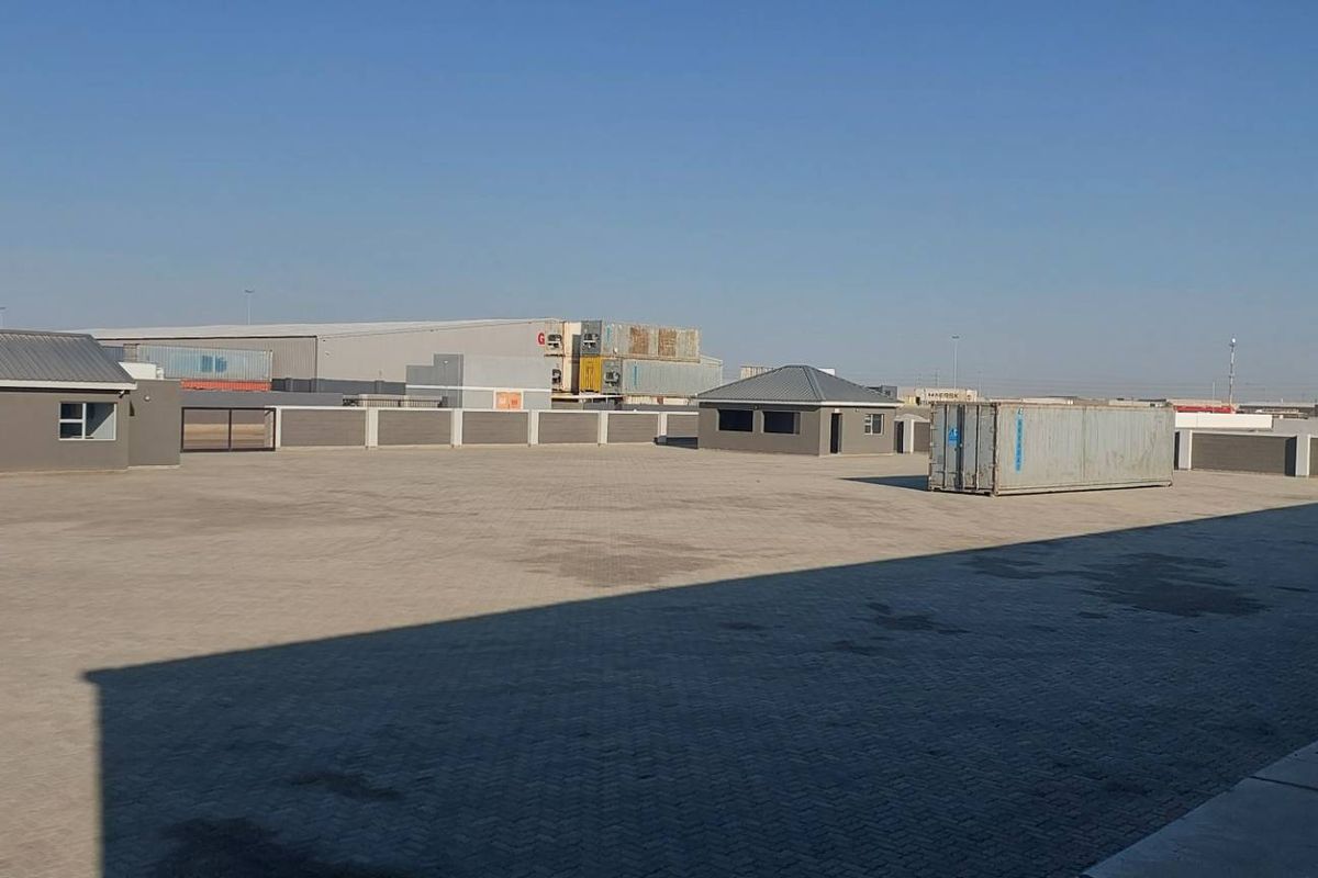 Expansive paved industrial yard featuring a perimeter wall, security gate, and auxiliary structures, providing ample space for logistics or storage operations.