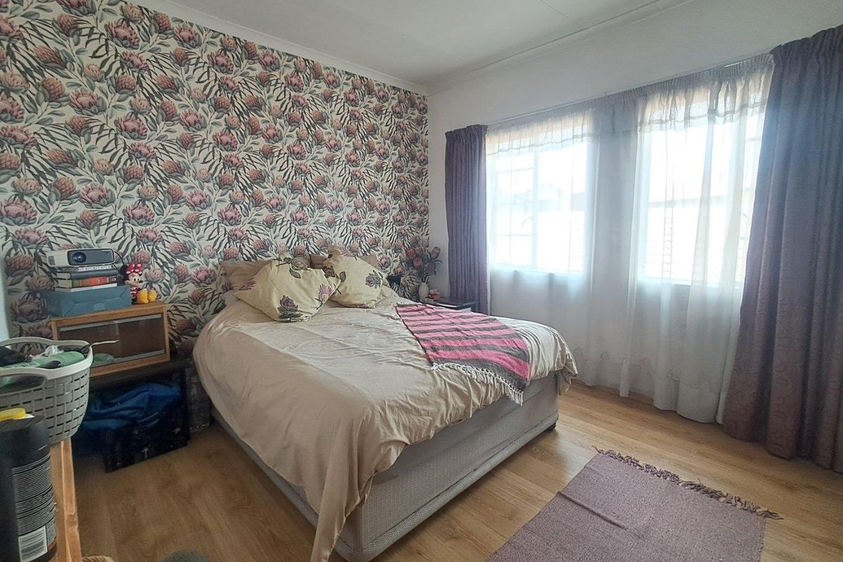A bedroom featuring laminate flooring, large windows allowing natural light, and a decorative floral feature wall.