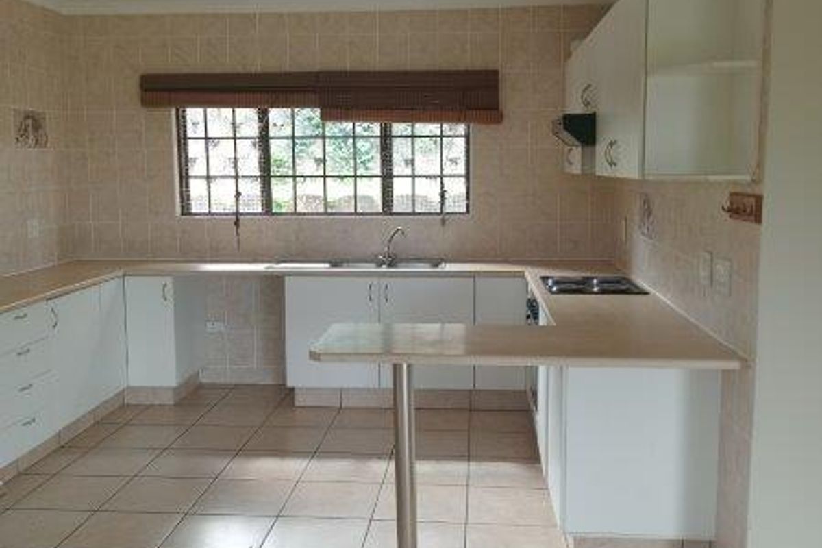 A spacious, empty kitchen featuring tiled flooring, ample built-in cabinetry, a breakfast bar, and a built-in hob with an extractor fan.