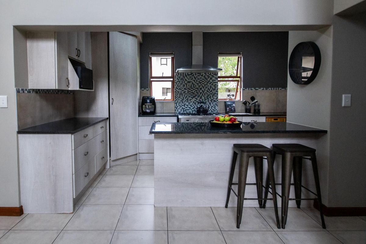 Modern kitchen featuring light wood cabinetry, dark granite countertops, a breakfast bar, and a tiled backsplash with a stainless steel extractor fan.