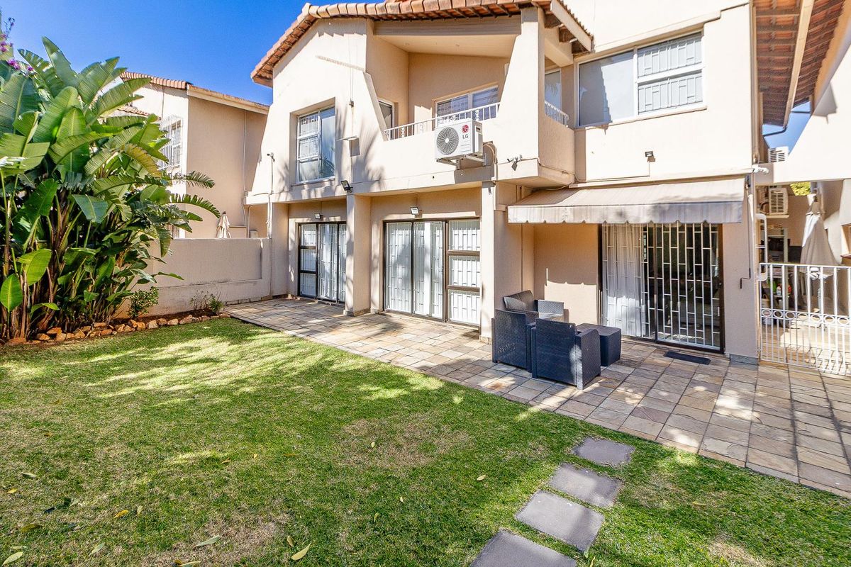 Rear view of the townhouse featuring a paved patio area, retractable awning, sliding glass doors with security gates, and a private garden.