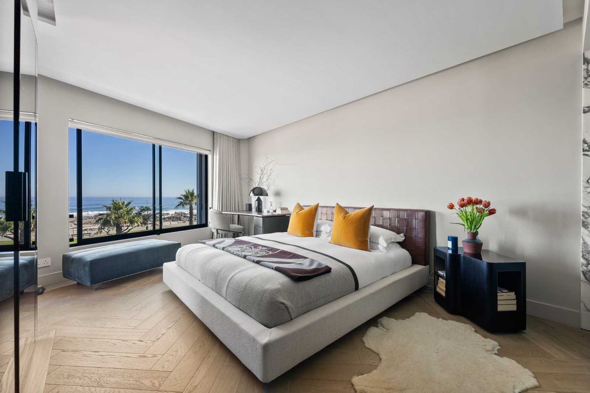 A modern, well-appointed bedroom featuring light oak herringbone flooring, large floor-to-ceiling windows, and expansive ocean views.