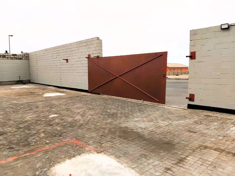 Industrial property entrance featuring a large sliding metal gate, cinder block boundary walls, and a paved driveway area.