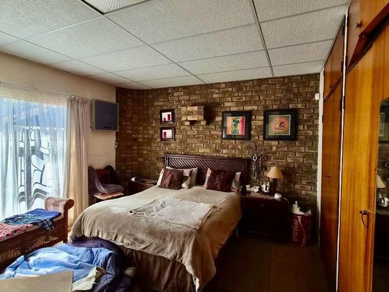 Bedroom featuring an exposed brick wall, built-in wooden cabinetry, and a drop ceiling, offering a dated aesthetic with potential for modernization.