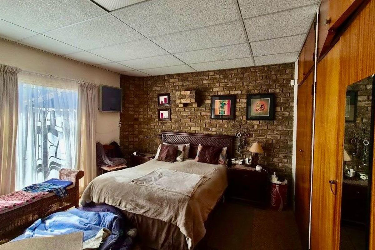 Bedroom featuring an exposed brick wall, built-in wooden cabinetry, and a drop ceiling, offering a dated aesthetic with potential for modernization.
