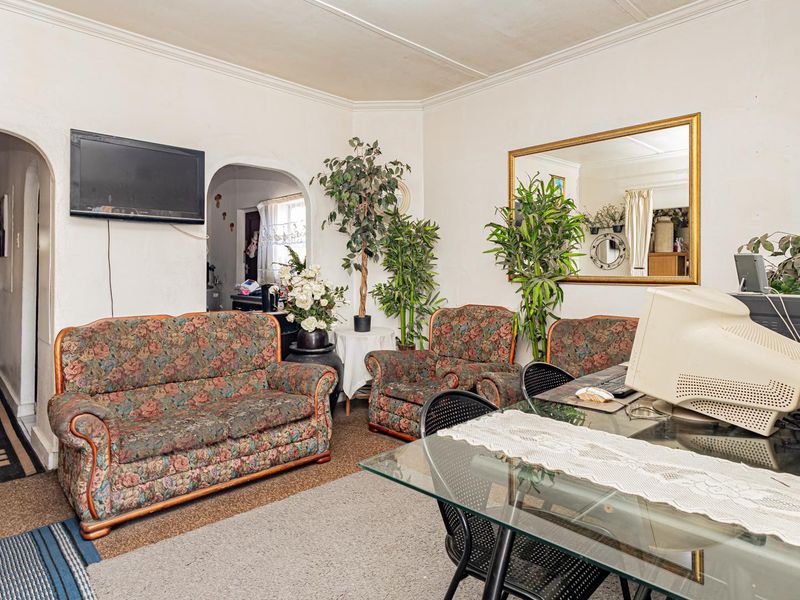 A living room featuring an arched entryway, coved ceilings, and carpeted flooring, offering a functional space with potential for modernization.