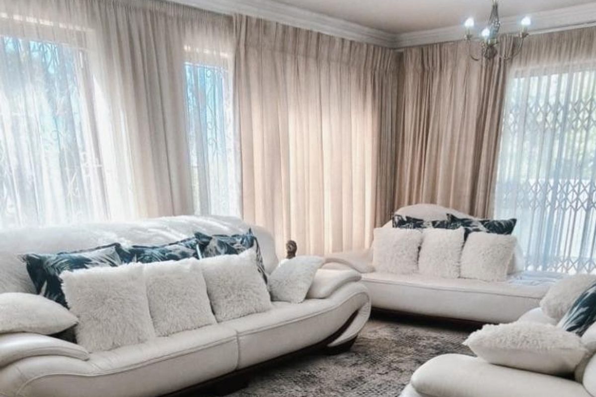 A bright and comfortable living room featuring crown molding, elegant sheer curtains, and classic chandeliers, creating a warm and inviting atmosphere.