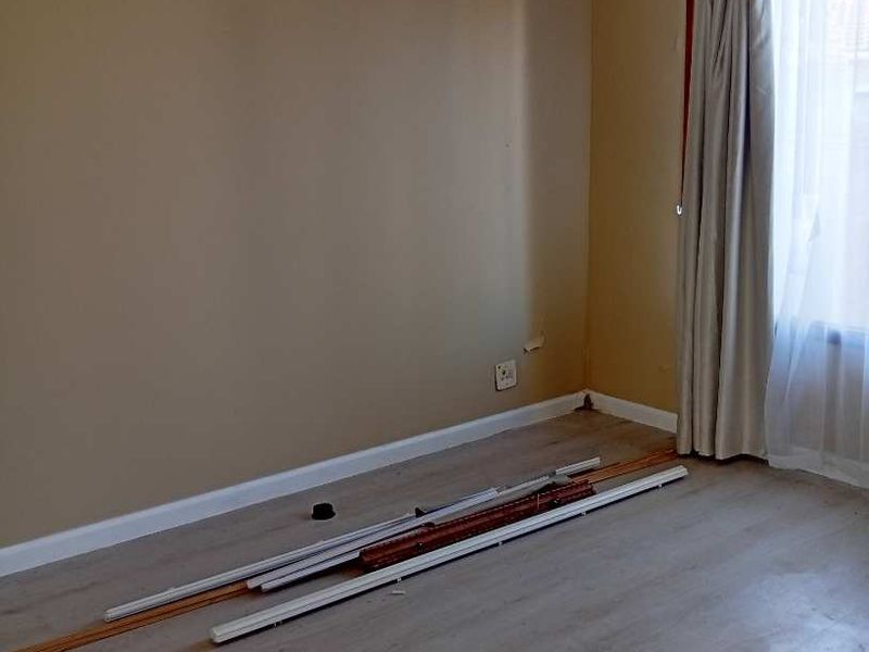 An empty bedroom featuring light-toned laminate flooring, neutral wall paint, and a window with installed curtain tracks.