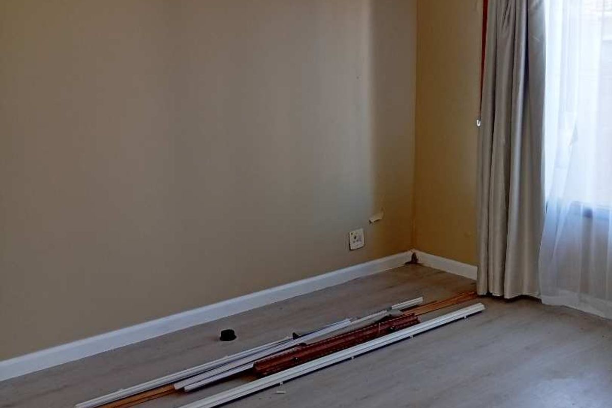An empty bedroom featuring light-toned laminate flooring, neutral wall paint, and a window with installed curtain tracks.