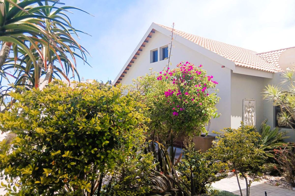A view of the rear exterior of the house featuring a gable roof, tiled roofing, and a paved walkway surrounded by established garden landscaping.