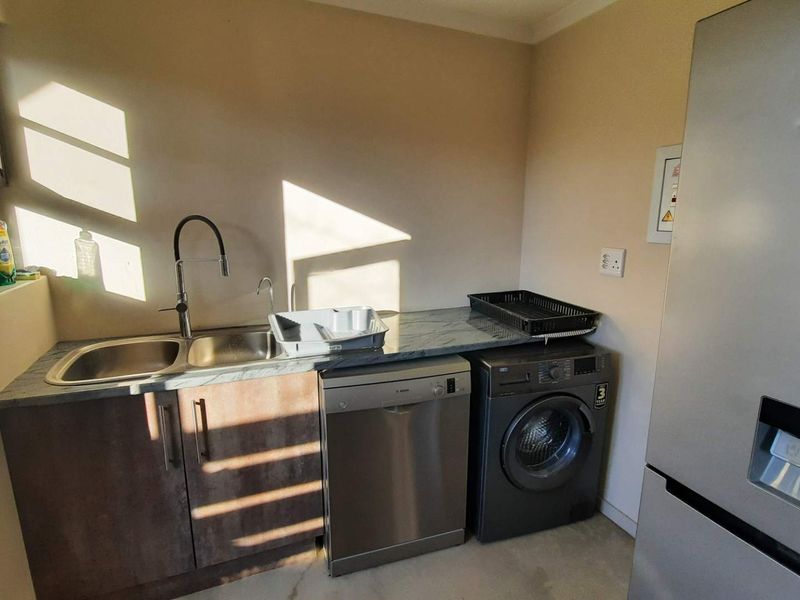 A functional laundry area featuring a stainless steel sink, laminate countertop, base cabinetry, and dedicated spaces for a dishwasher and washing machine.