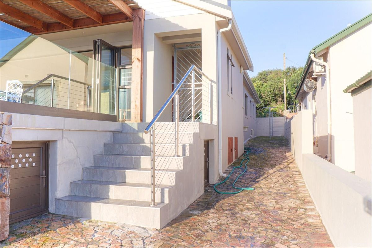 Side exterior view featuring a stone-paved pathway, tiled staircase with stainless steel railing, and a covered patio area with glass balustrades.