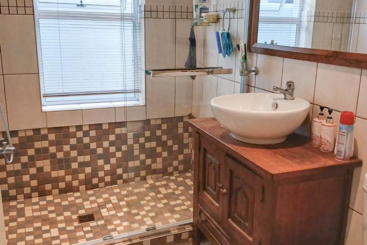 A functional bathroom featuring a walk-in shower with mosaic tiling, a wooden vanity cabinet with a vessel sink, and a large framed mirror.