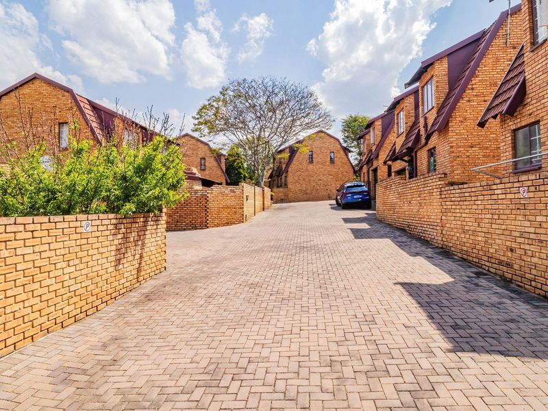 A view of the townhouse complex driveway featuring brick-paved access and established brick-faced residential units.