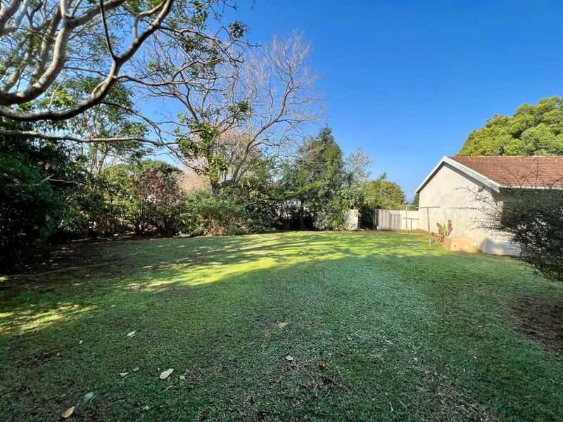 A spacious, level backyard featuring a well-established lawn, mature trees, and perimeter fencing, offering a private outdoor space.