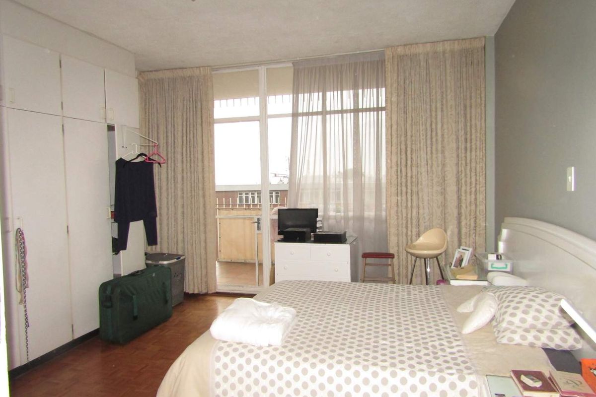 A bedroom featuring built-in cupboards, parquet flooring, and direct access to a private balcony through large glass doors.