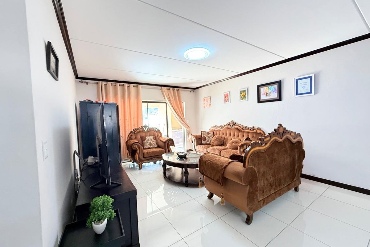 A bright living room featuring polished white floor tiles, a drop ceiling with integrated lighting, and sliding glass doors leading to an outdoor area.