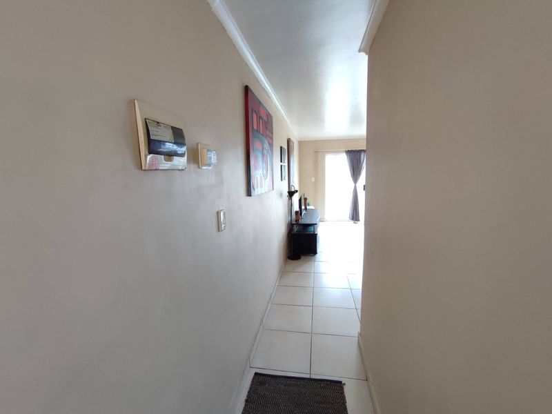 A bright hallway featuring tiled flooring and coved ceilings, leading towards a sliding glass door that provides access to the outdoor area.