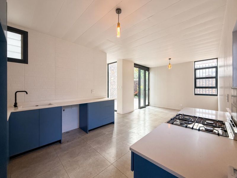 Modern open-plan kitchen and living area featuring blue cabinetry, stone countertops, gas hob, and direct access to the outdoor patio through sliding glass doors.