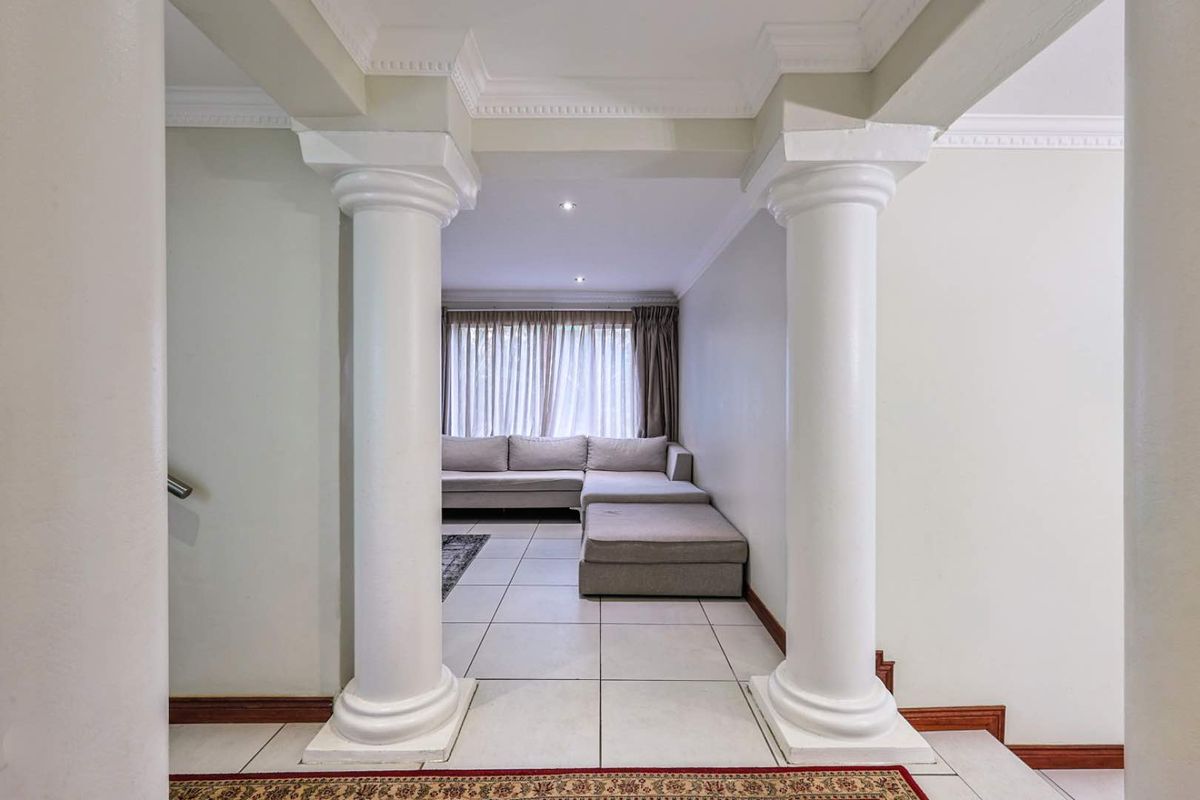 A view through a classic columned archway into a tiled living area featuring recessed ceiling lighting and neutral wall finishes.