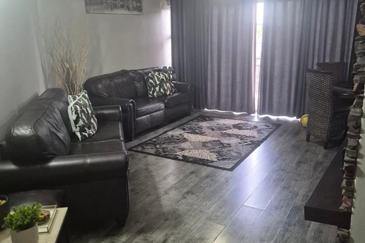 A living room featuring high ceilings, dark wood-look laminate flooring, and a stone-clad fireplace feature wall with access to an outdoor area.