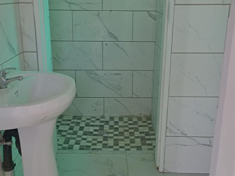 A compact bathroom featuring a pedestal washbasin with chrome tapware and a shower area finished with marble-look wall tiles and mosaic floor tiling.