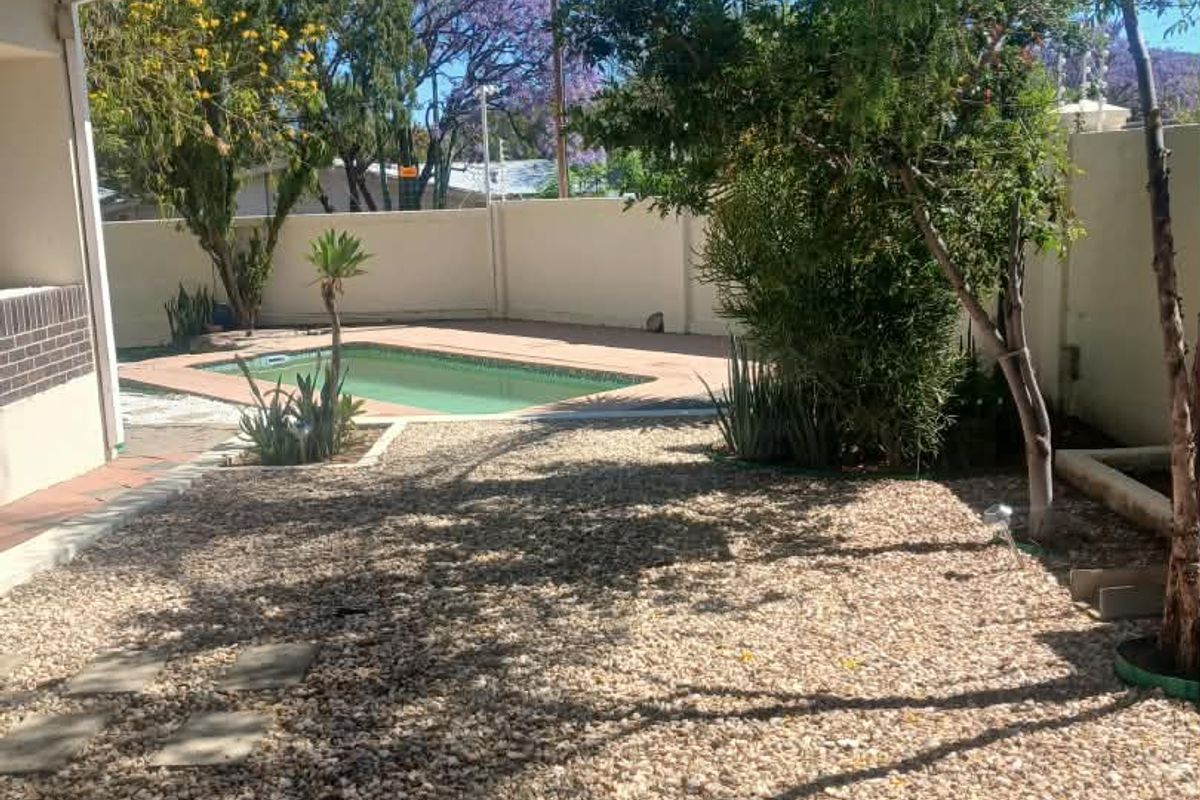 A private backyard featuring a swimming pool with a paved surround, gravel landscaping, and perimeter walling.