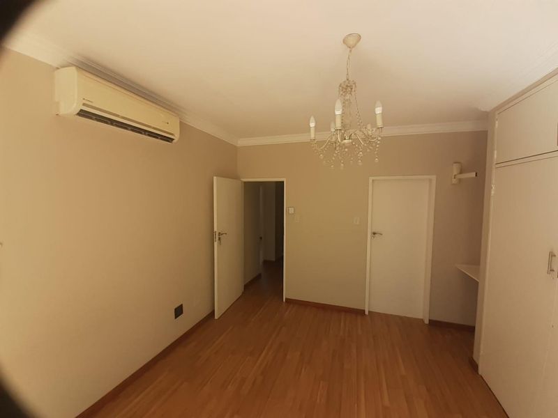 A spacious, empty bedroom featuring laminate flooring, built-in cupboards, an air conditioning unit, and a decorative chandelier.