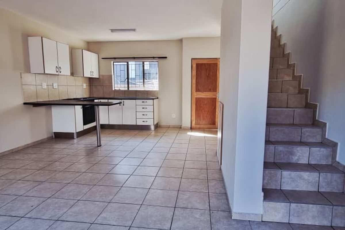 An open-plan living and kitchen area featuring tiled flooring, built-in cabinetry, and a tiled staircase leading to the upper level.