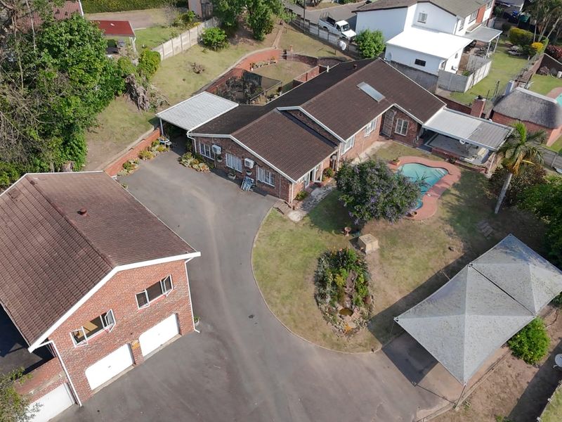 Aerial view of a residential property featuring a main house, detached double garage, swimming pool, paved driveway, and established garden areas.
