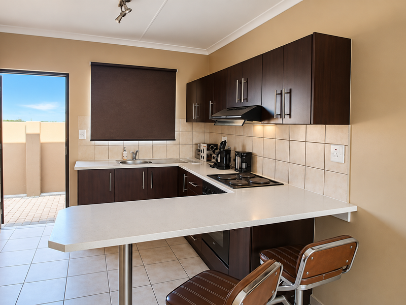 A functional kitchen featuring dark wood cabinetry, white countertops, built-in appliances, and direct access to an outdoor patio area.