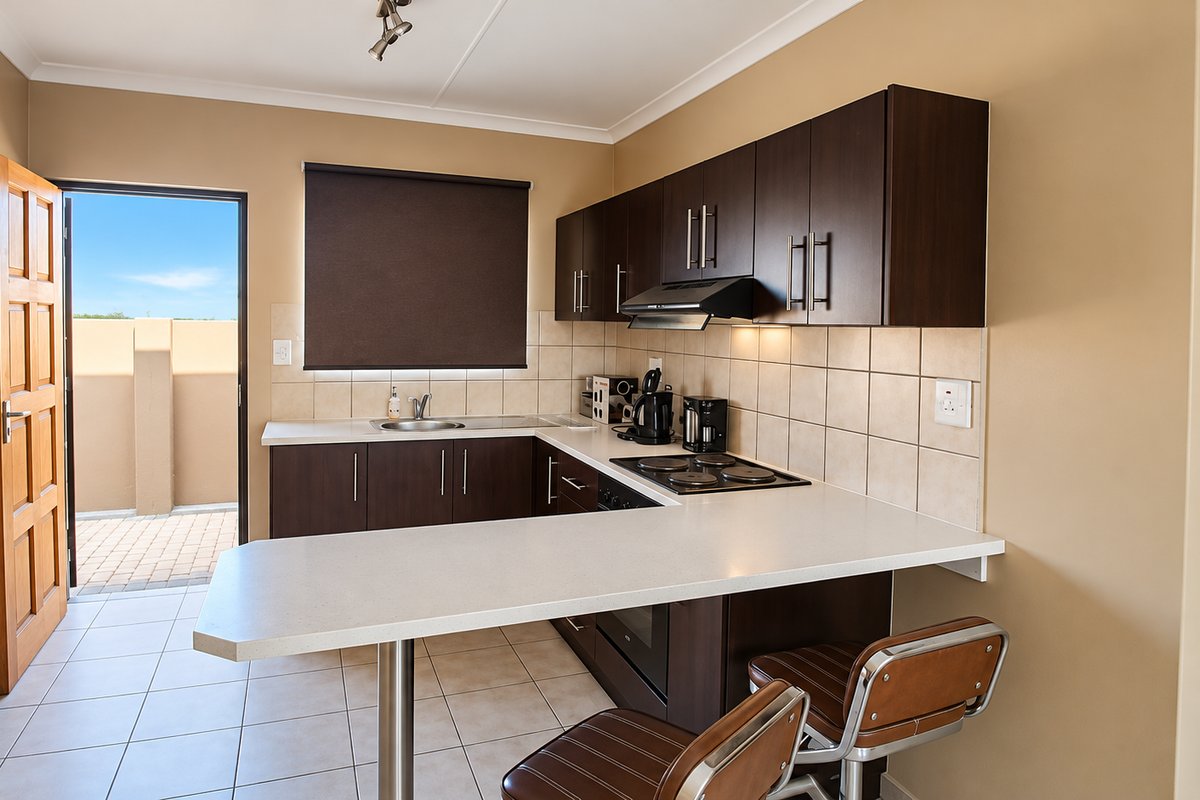 A functional kitchen featuring dark wood cabinetry, white countertops, built-in appliances, and direct access to an outdoor patio area.