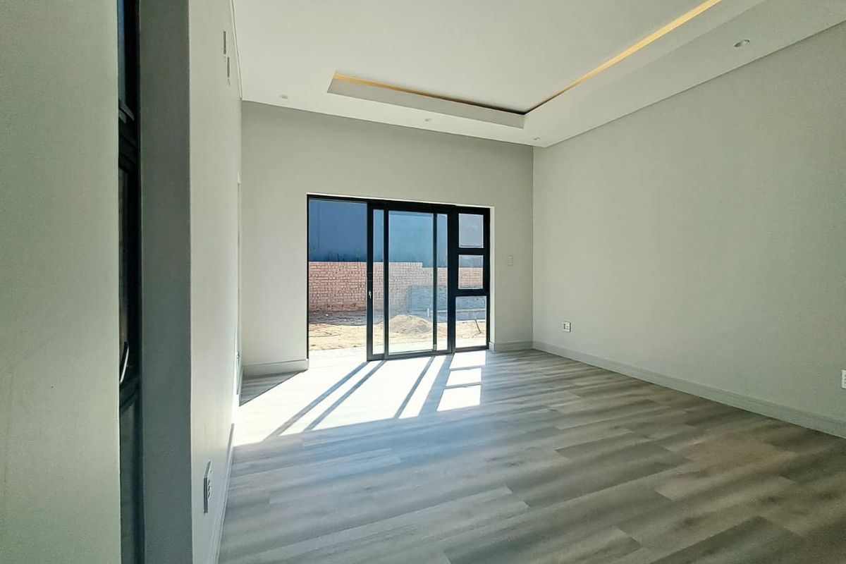 A bright, modern, and empty living room featuring laminate flooring, a recessed ceiling with cove lighting, and a large sliding glass door.