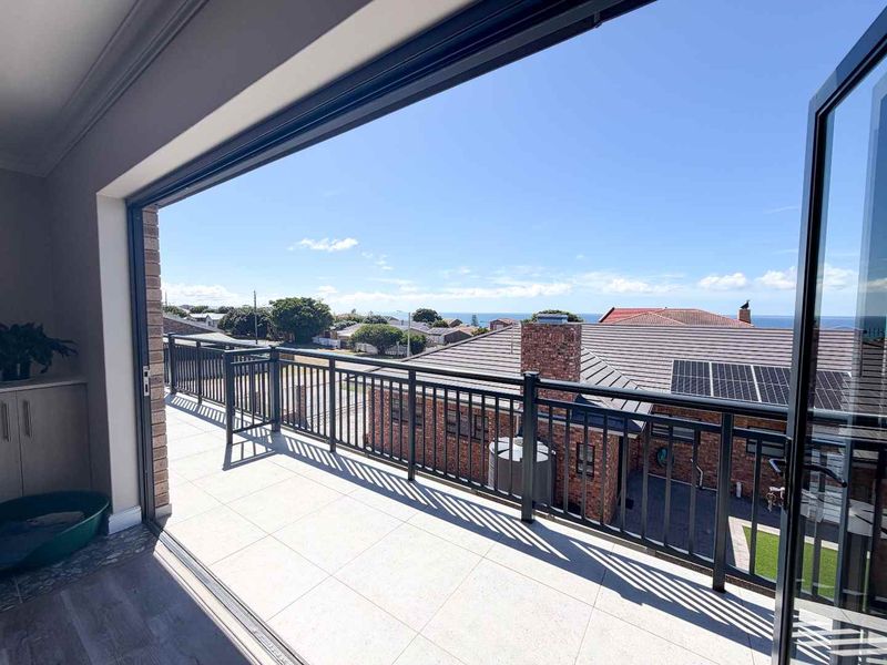 Spacious elevated balcony featuring tiled flooring, modern metal balustrades, and wide stacking doors offering expansive coastal and neighbourhood views.