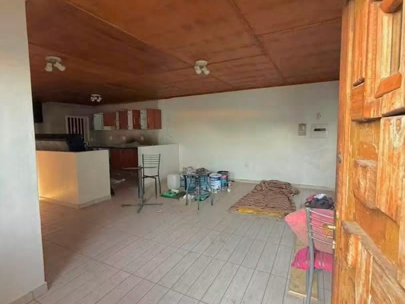 Open plan living and kitchen area featuring tiled flooring and a wooden panel ceiling, currently vacant and in need of cosmetic updates.